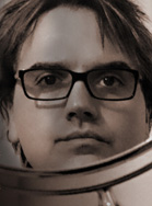 Close-up portrait of a person with dark hair and black-rimmed glasses looking forward.