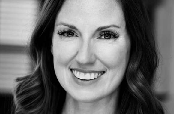 Black and white close-up portrait of a woman with wavy hair smiling at the camera.