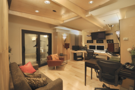 A recording studio with wooden ceilings, a mixing console, computer monitors, and a lounge area.