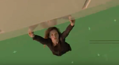 A woman with curly hair hangs from a light-colored surface against a solid green background.