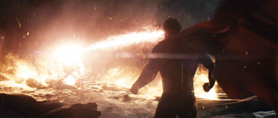 A person in a cape stands in a dark, smoky environment facing a bright, horizontal blast of fire and light.