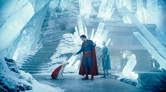 Superman in costume stands in an icy crystal fortress next to a white dog wearing a red cape.