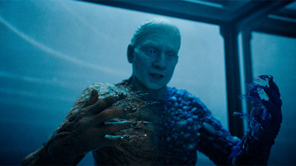 A pale, textured humanoid figure with blue and brown skin looks down at its clawed hands.