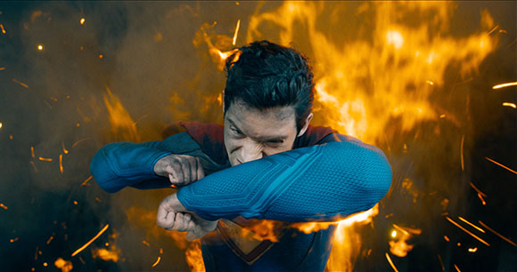 A man in a blue suit braces for impact amidst swirling orange flames and sparks.
