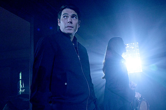 A man in a dark jacket looks up toward a bright light source in a dark room.