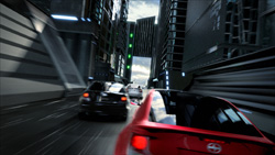 A red car and a black car speed through a narrow street between tall, dark skyscrapers.