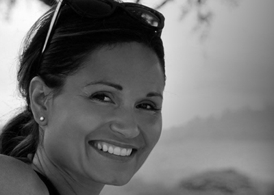 Black and white close-up portrait of a smiling woman with sunglasses on her head.