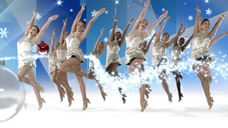 Group of female dancers in silver sequined dresses performing a synchronized dance with sparkling light effects.