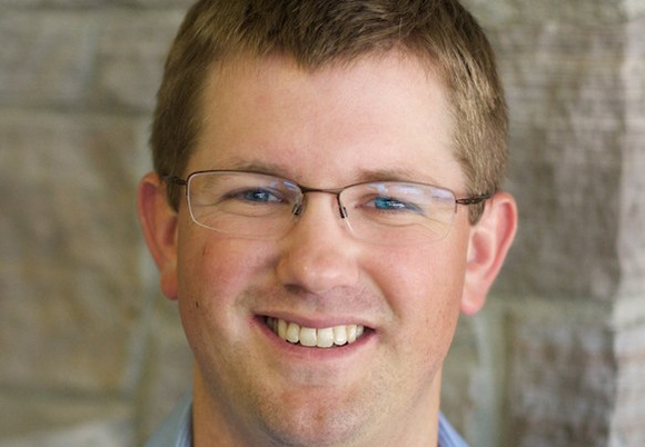 Close-up of a man with short brown hair and glasses, smiling.