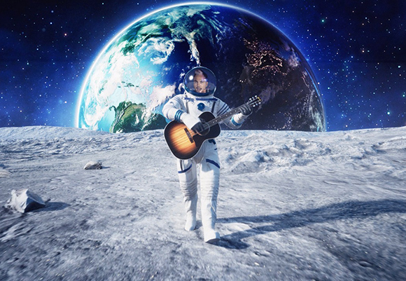 An astronaut in a white spacesuit plays an acoustic guitar on the lunar surface with Earth rising behind them.