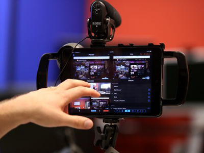 A person's hand touches a tablet screen displaying video preview feeds on a professional camera rig.