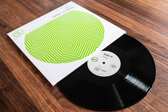 A black vinyl record partially pulled out of a white sleeve with a green geometric pattern.