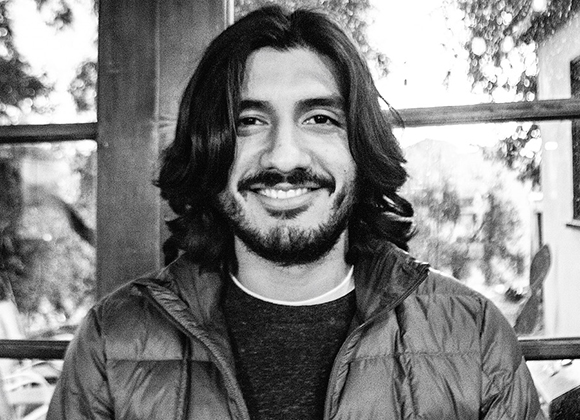 Black and white portrait of a smiling man with dark, shoulder-length hair and a beard.