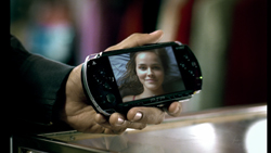 A person holds a small black handheld device showing a smiling woman on its screen.