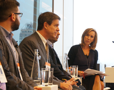 Four people sit in a row at a panel discussion in a bright room with large windows.