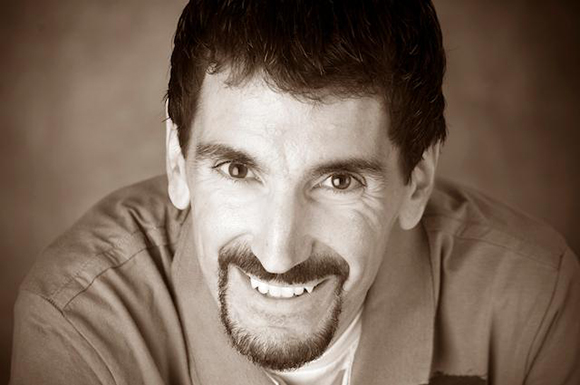 A sepia-toned close-up portrait of a man smiling at the camera.