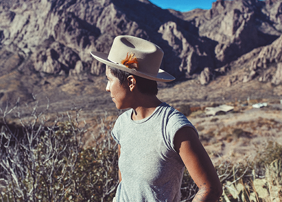 A person wearing a tan wide-brimmed hat with a feather, looking toward a rocky mountain range.