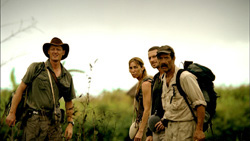 Four people in outdoor gear standing in a grassy field under an overcast sky.