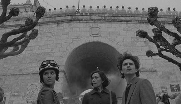 Black and white shot of three people looking upward in front of a massive stone archway and trees.