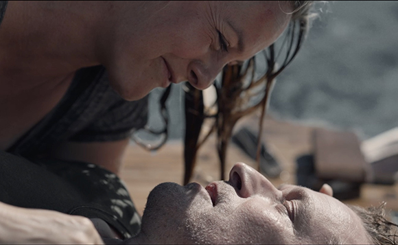 A woman leans down close to a man's face as he lies on his back.