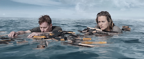 A man and a woman float in dark blue ocean water amidst a large collection of floating books.