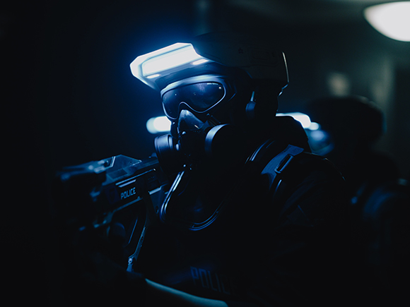 A person wearing a tactical mask, goggles, and helmet in a dark, blue-toned setting.