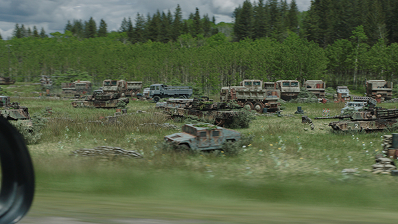 Multiple rusted and overgrown military trucks and armored vehicles scattered in a green field.
