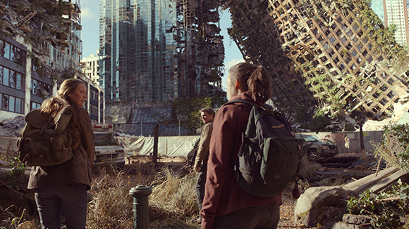 Two people with backpacks look at collapsed, debris-filled skyscrapers in a destroyed city.