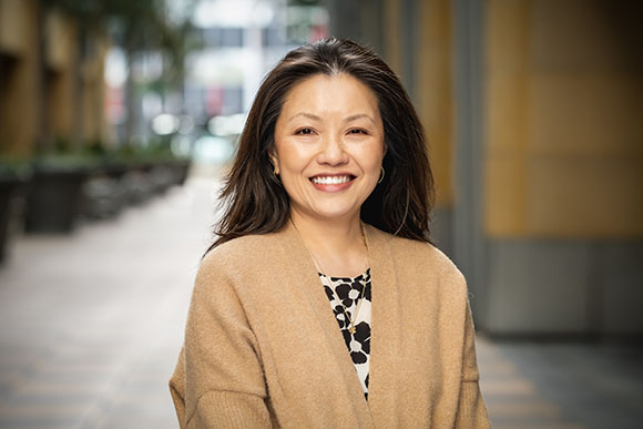 A smiling woman with dark hair wearing a tan cardigan and a patterned blouse.