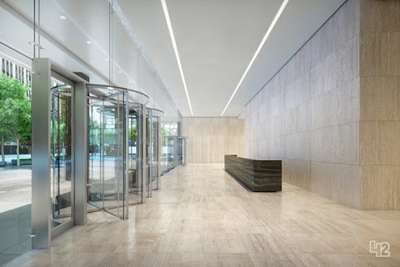 A bright, modern building lobby with glass revolving doors, stone walls, and light wood flooring.