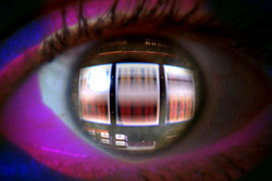 Close-up of a human eye reflecting a glowing, multi-paneled digital screen with red and blue light.