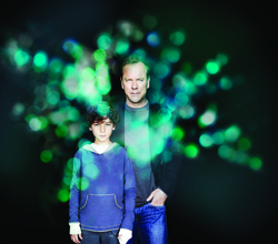 A man and a young boy pose together against a dark background filled with glowing green bokeh lights.