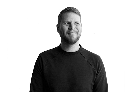 Black and white portrait of a man with a beard wearing a dark sweatshirt, looking to the side.