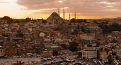 Aerial view of a city skyline with a large domed mosque and several minarets under a sunset sky.