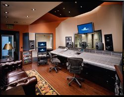 A professional recording studio featuring a large mixing console, studio monitors, and leather seating.