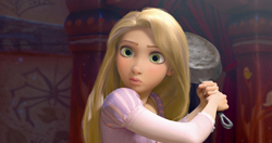 A blonde woman with large green eyes holds a heavy frying pan with both hands.