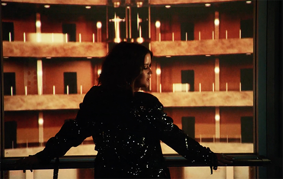 Silhouette of a woman in a sequined jacket standing before a warm, glowing multi-tiered structure.