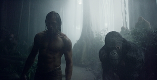 A shirtless man and a large gorilla walk through a dark, misty jungle setting.