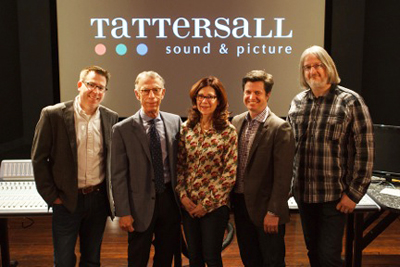 Five people standing in a row in front of a large screen displaying the Tattersall sound & picture logo.