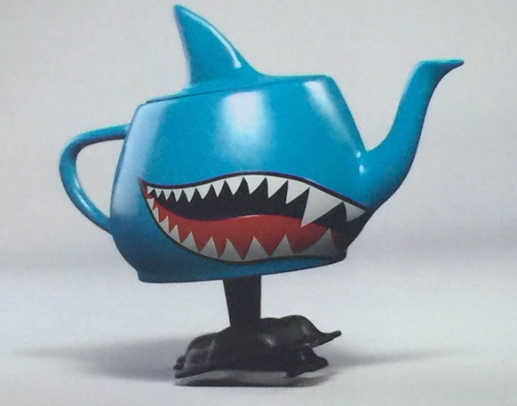 A blue teapot shaped like a shark with a gaping mouth and sharp teeth, resting on a black base.