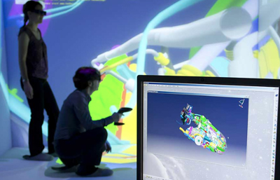 Two people using VR headsets to interact with a large, colorful 3D digital model projected on a wall.