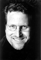 A black and white close-up portrait of a smiling man wearing glasses.