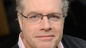 Close-up portrait of a man with light hair and thin-rimmed glasses looking forward.