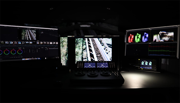 Multiple computer monitors displaying video editing software and color grading tools in a dark studio.