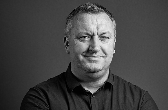 Black and white headshot of a middle-aged man with short hair wearing a dark button-down shirt.