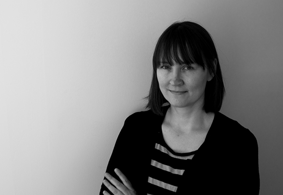Black and white portrait of a woman with shoulder-length hair and bangs, wearing a striped shirt and dark cardigan.