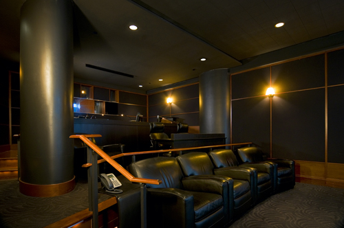 A dark courtroom featuring rows of black leather chairs, large dark pillars, and wood-paneled walls.