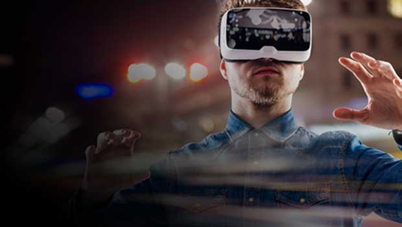 A man in a denim shirt wears a white VR headset and gestures with his hands against a blurred night background.