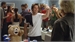A man in a white t-shirt dances in a crowded room near a large teddy bear.