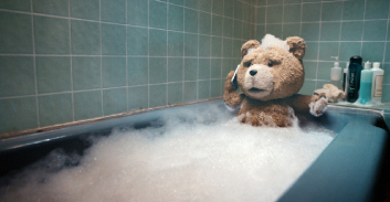 A brown teddy bear sitting in a bathtub filled with white soap bubbles.